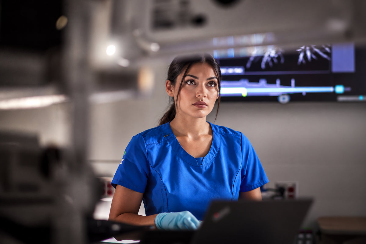 Zorgmedewerker werkt op een laptop bij een monitor met patientgegevens