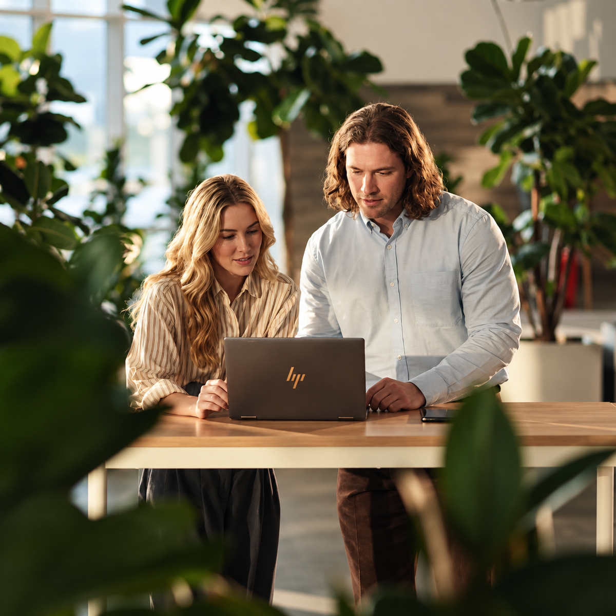 Twee collega's kijken samen naar een laptop aan een hoge tafel in een kantoor met planten